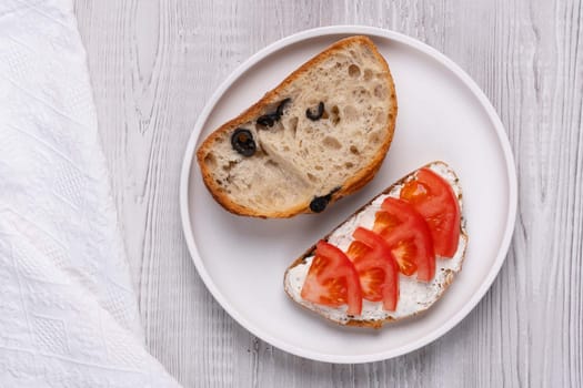 Slice of bread with cottage cheese and tomatoes on a white wooden background.