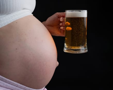 Close-up of the belly of a pregnant woman holding a glass of beer on a black background. Skin rash