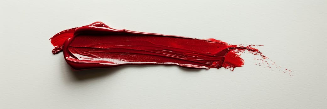 A close-up of a lipstick smudge on a pristine white surface, showcasing a bold matte red hue.