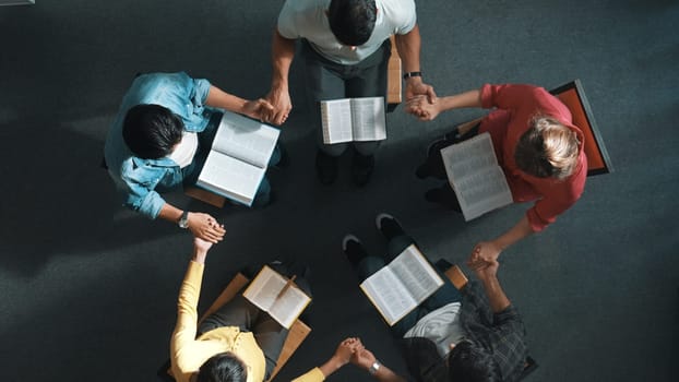 Top down view of diverse people holding hand and sitting in circle with bible book on lap. Aerial view of faithful prayer clasp hand and praying to god with faith, religion conceptional. Symposium.