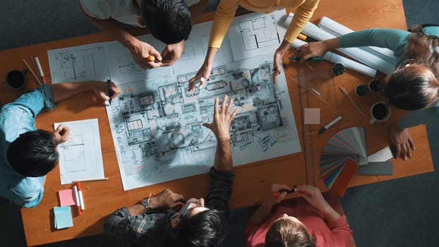 Top down view of civil engineer team writing at blueprint at meeting table with color palettes. Group of diverse people planning and taking a note while manager looking at project plans. Symposium.