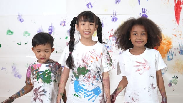 Diverse students put hands up together show colorful stained hands. Group of multicultural learner standing at white background with stained hands while looking at camera in lively mood. Erudition.