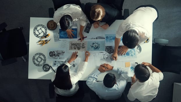 Top down aerial view of smart engineer team working together to design turbine engine. Professional technician discussing about jet engine construction while pointing at part of engine. Alimentation.