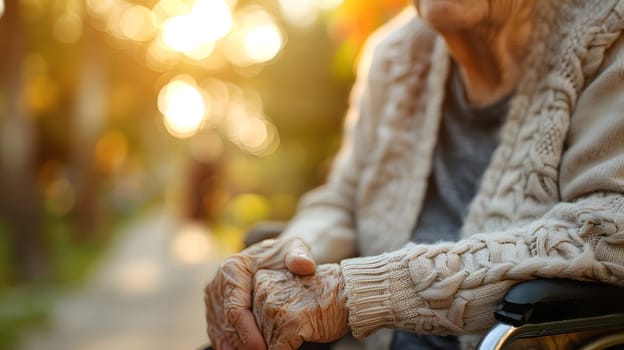 An elderly woman is sitting in a wheelchair, holding her hands together with a gesture of happiness. Her fingers are intertwined and her thumb rests on her wooden armrest