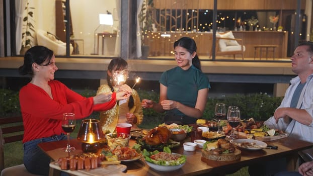 Happy family holding glowed sparkler in holiday celebration party at night. Lovely member enjoy playing spark toy together. Outdoor activity to cross generation gap strengthen family bond. Divergence.