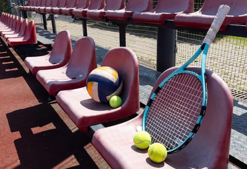 a tennis racket, balls and a volleyball on a bench on the sports tribune. High quality photo