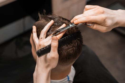 Top view barber uses scissors and comb to style the mans hair at the barbershop