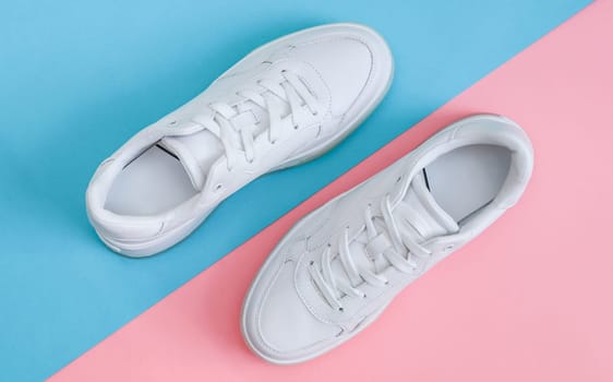 One pair of white sneakers lie diagonally on a pink-blue flat lay background close-up. The concept of fashion, beauty, shoes.