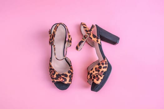 One pair of female tiger print platform sandals with heels lies in the center on a pink flat lay background. The concept of fashion, beauty, shoes.