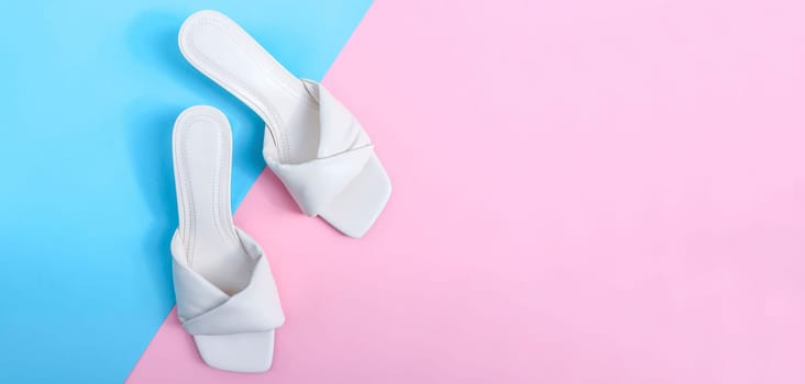 One pair of white female heeled flip flops lie to the left against a blue-pink background with copy space to the right of the flat lay close-up. The concept of fashion, beauty, shoes.