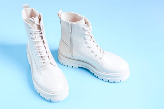 White demi-season boots made of eco-leather with a rough sole and lacing on a blue background, close-up side view. The concept of fashionable women's shoes.