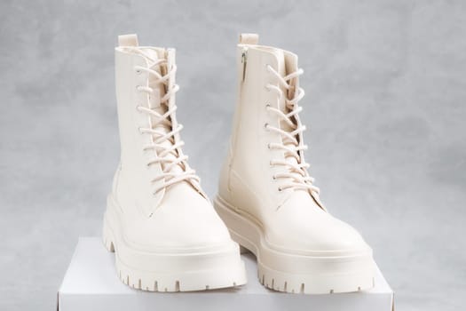 White demi-season boots made of eco-leather with fasteners, laces stand on a white cardboard box on a gray cement background, close-up side view. The concept of fashion and women's shoes.