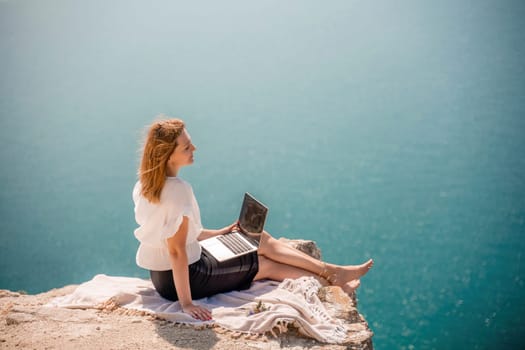 Freelance woman working on a laptop by the sea, typing away on the keyboard while enjoying the beautiful view, highlighting the idea of remote work