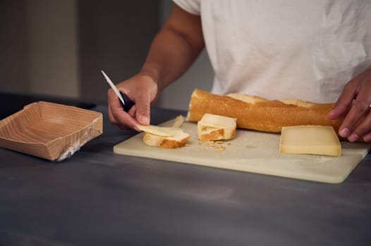Close-up hands of a woman in white t-shirt, putting a slice of cheese over piece of bread, preparing sandwiches for snack