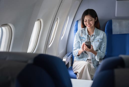 Asian woman using smartphone on airplane. Concept of travel, technology, and leisure.