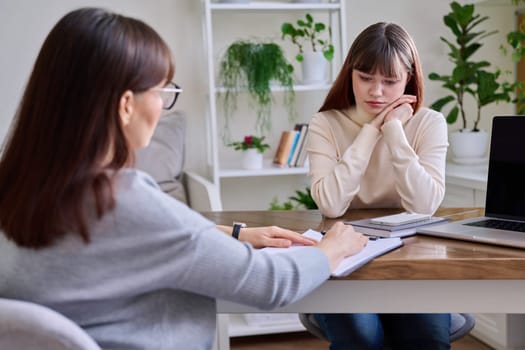 Sad upset teenage girl talking to psychotherapist psychologist counselor at therapy session in specialist office. Mental health of youth, social services for mental support, psychological counseling