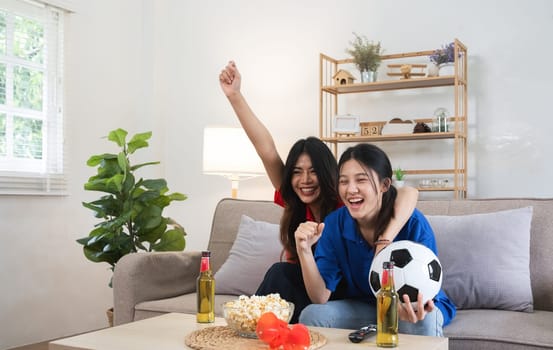 A lesbian couple cheers football and celebrate together for their favorite Euro football team. A young female couple cheers football on TV together in the living room on match day..