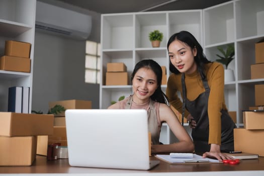 Two women working on laptop and packing boxes in warehouse.