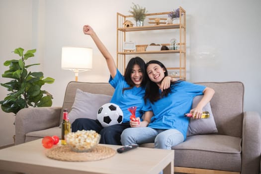 A lesbian couple cheers football and celebrate together for their favorite Euro football team. A young female couple cheers football on TV together in the living room on match day..