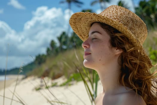 Woman in straw hat relaxing on beach with eyes closed looking up at sky in serene beauty and tranquility