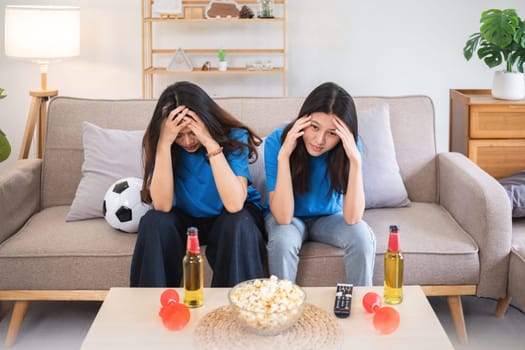 Asian women watching soccer game at home with disappointment. Concept of sports, emotions, and friendship.