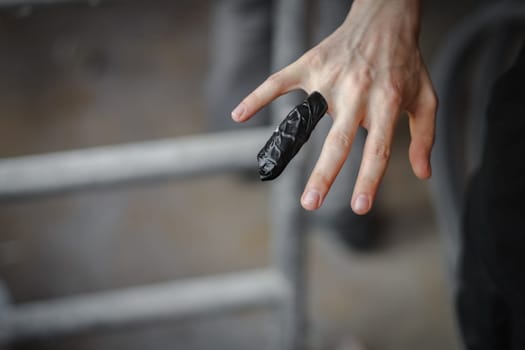 The hand of a Caucasian young male with a bandaged injured finger with black tape from damage during construction work, close-up side view with selective focus. The concept of home renovation, a wound on the finger.