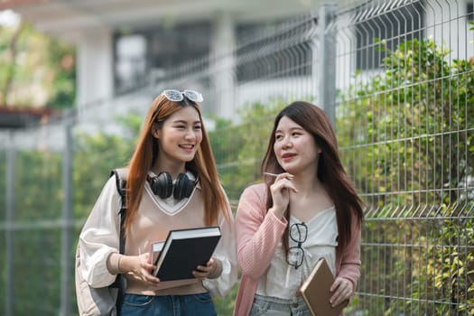 Two university female students walking and chatting on campus. Friends discussing studies and carrying books. Concept of education, friendship, and student life.