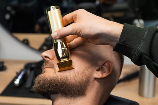 Barber trims the beard on the clients cheek, using the trimmer to achieve a clean and sharp line.