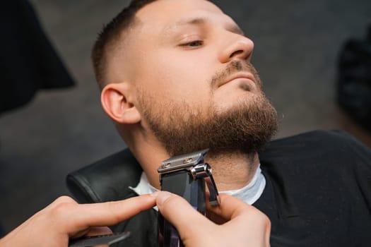 Man during the procedure of cutting beard in the barbershop.