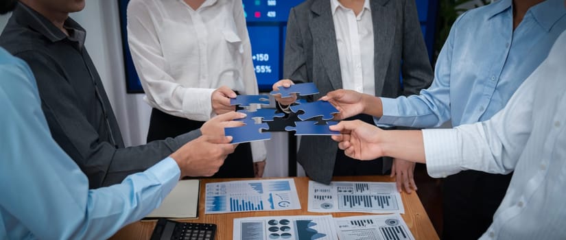 Corporate officer worker collaborate in office, connecting puzzle pieces with report paper on table as partnership and teamwork. Unity and synergy in business concept by merging jigsaw puzzle. Concord