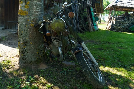 Kretinga, Lithuania - August 12, 2023: A motorcycle Jawa stands parked next to a tree in a grassy yard under the sun.