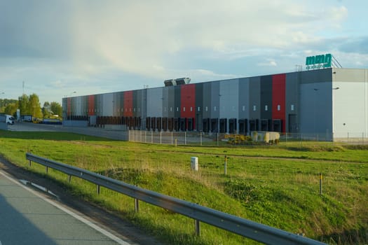 Pasvalys, Lithuania - May 3, 2023: A large, modern warehouse with MMG Service signage is situated in a rural area, bathed in sunlight and featuring a colorful facade.