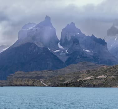 Dramatic mountains rise above a calm turquoise lake under moody skies.