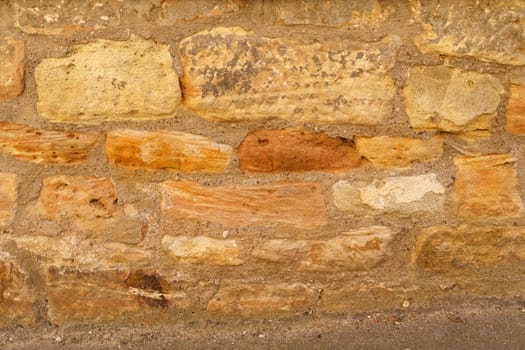 A weathered stone wall with patches of paint peeling off, showcasing a blend of textures and colors.