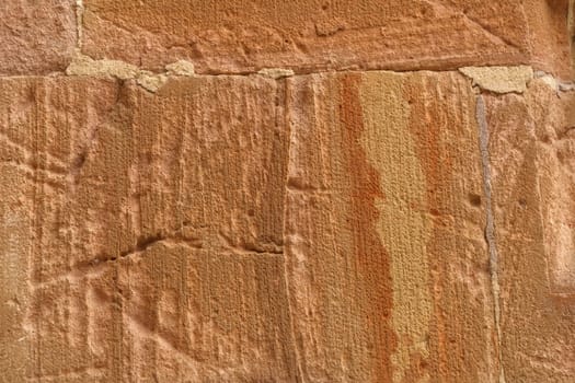 Detailed close-up view of a brick wall with vibrant red paint peeling off, revealing the rough texture of the stone beneath.