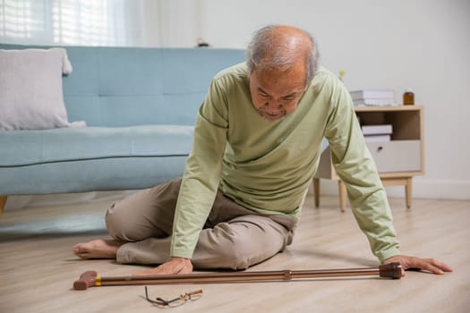 Sick senior old man falling down lying on floor because stumbled at home alone with wooden cane walking stick in living room, elderly man retired grandfather having accident after standing from sofa