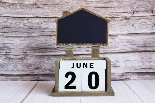 Chalkboard with June 20 calendar date on white cube block on wooden table.