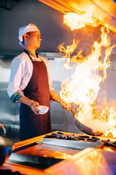 In professional kitchen chef hands handle flaming wok. Closeup of cooking expertise flames at work. Skillful chef burning food working in a modern kitchen setup. cook food with fire
