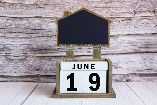 Chalkboard with June 19 calendar date on white cube block on wooden table.