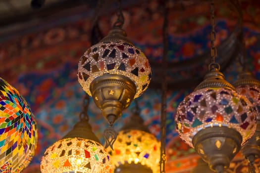 Middle Eastern lambas of different colors and sizes are hanging in the bazaar. Bright traditional Arabic and Turkish lanterns made of metal and glass, inlaid with mosaic details of different colors.