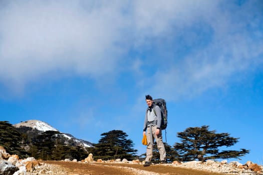 Young man travels, walks along a trail among the mountains with tourist equipment, the traveler stands against the background of a bright blue sky on the way to the top of the hill.