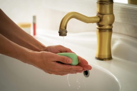 A young girl washes her hands thoroughly with soap under water in the bathroom, close-up view.