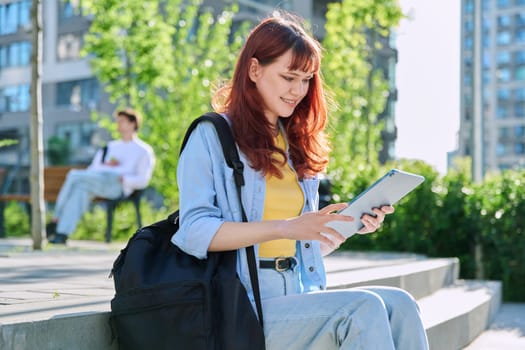 Young attractive female college student using digital tablet outdoor, educational building background. Education, technology, training, 19,20 years age youth concept