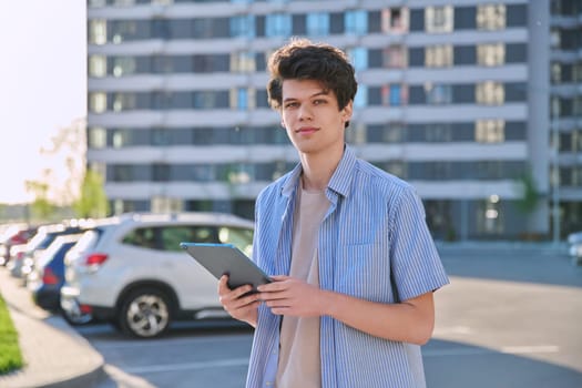 Young male using digital tablet on city street. Handsome guy student 19-20 years old, using pad for leisure, studying, working. Technology, youth, education, urban style concept