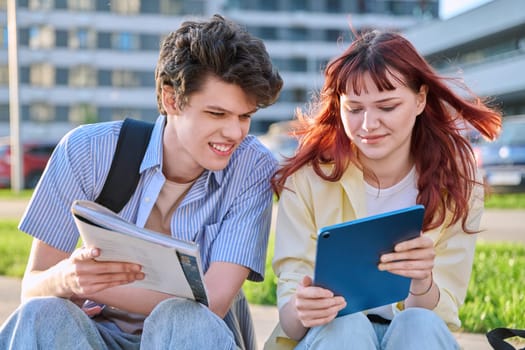 Teenage college students guy and girl talking, using digital tablet, sitting outdoor, urban modern city. Youth 19-20 years old, education, technologies, lifestyle, friendship concept