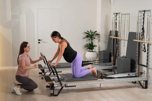 A pregnant woman works out on a reformer exercise machine with a personal trainer