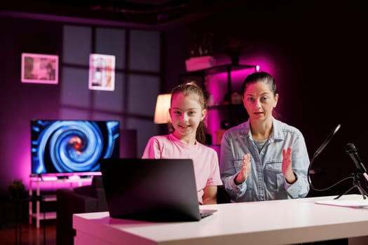 Daughter and mom filming reaction video for gen Z viewers, looking at online videos on laptop. Small child and her parent recording opinion on funny internet clips for family channel