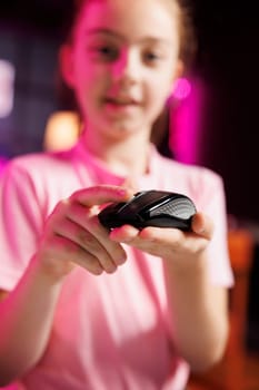 Close up shot of young media star in studio reviewing gaming mouse in front of camera in personal studio. Cheerful kid filming electronics haul, pressing buttons to test wireless computer peripheral