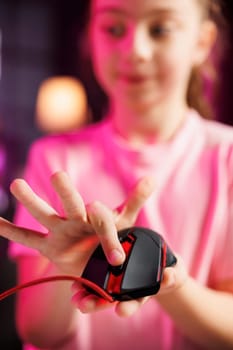 Close up shot on gaming mouse received by kid from sponsoring brand to promote it. Focus on wired computer peripheral advertised by young child in blurry background doing influencer marketing