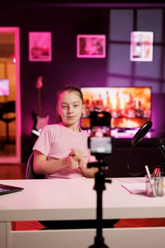 Girl being sponsored by partnering brand to showcase their message on children channel, filming with phone on tripod. Kid does influencer marketing, advertising new campaign, recording with smartphone